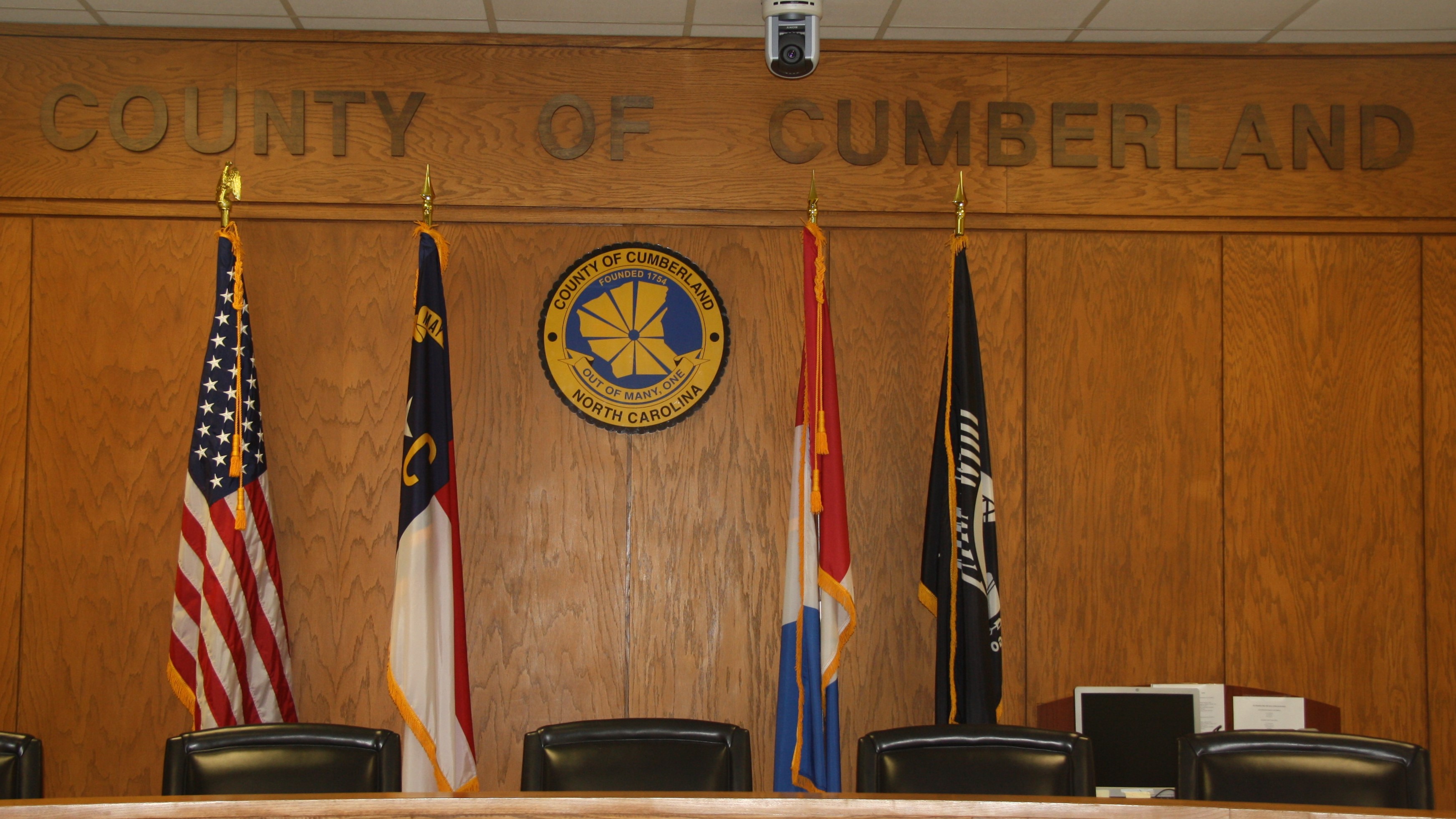 Commissioners' dais with County seal and flags in background.