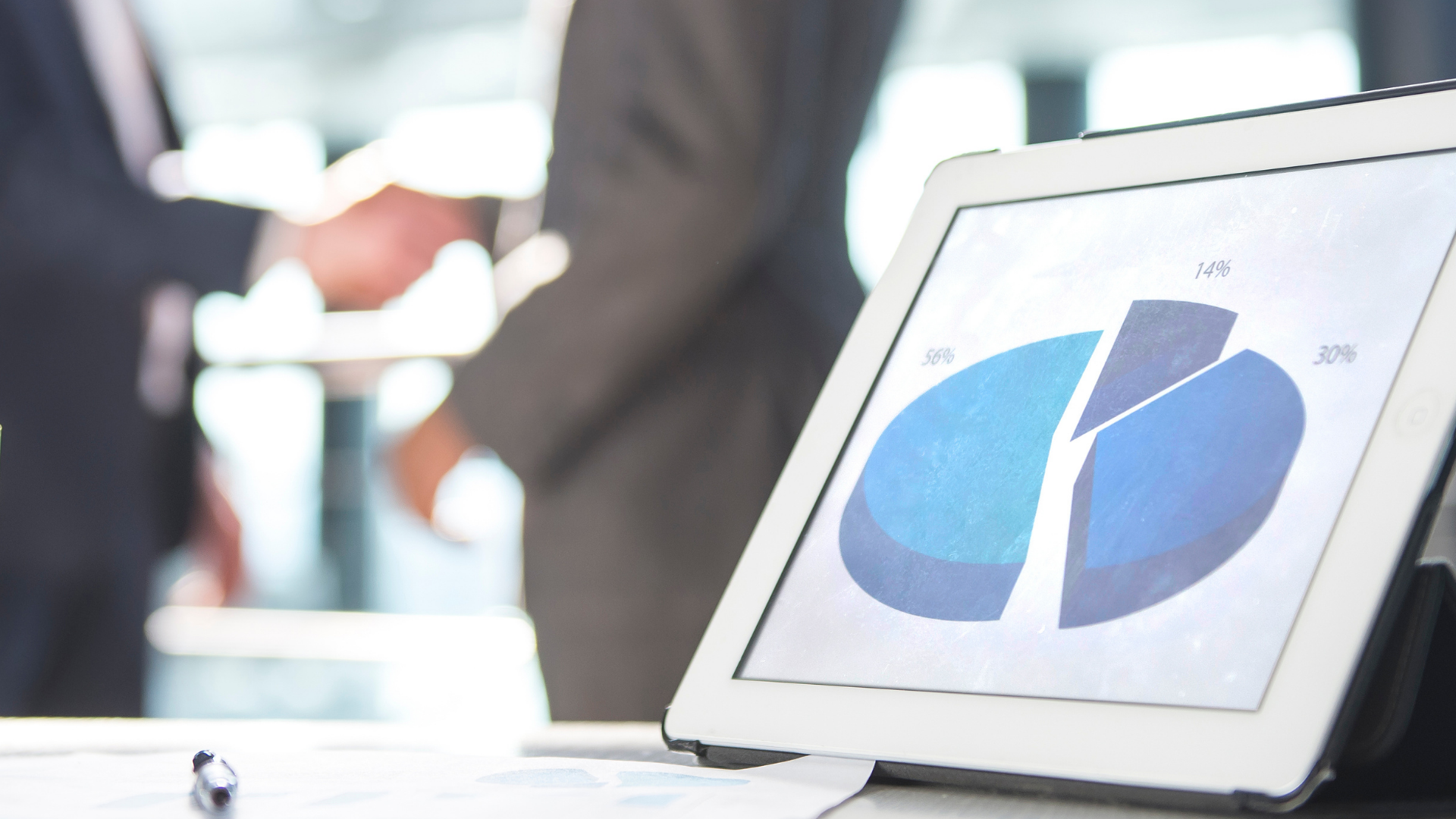 Close up of tablet displaying a pie chart and business people in background.