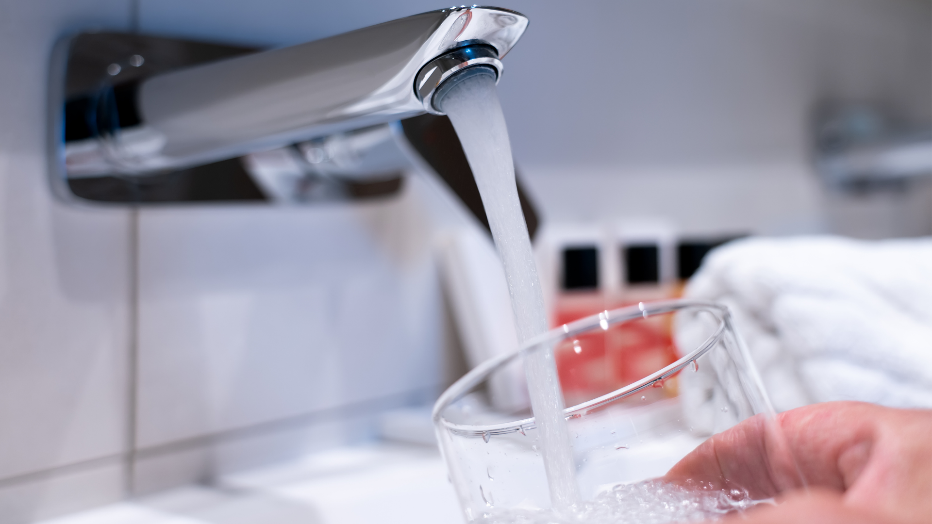 Person holding drinking glass under running kitchen faucet.
